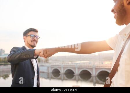 Primo piano di amici multietnici che fanno pugno mentre salutano ciascuno altro contro il ponte Foto Stock