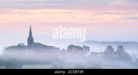 Il campanile della chiesa di St Barnaba a Weeton, Lower Wharfedale, è visibile sopra una coperta di nebbia estiva durante un'alba color pastello ad agosto. Foto Stock