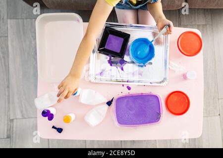 Dall'alto di raccolto anonimo capretto in abbigliamento casual seduto su un comodo divano davanti al tavolo con vassoio sporco e contenitori di plastica con miscela luminosa a casa Foto Stock