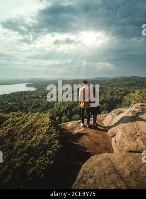 Vista posteriore di una coppia anonima di viaggiatori in piedi su pietra percorso tra piante verdi vicino al lago e godendo di uno scenario spettacolare In una giornata di sole mentre visitate il Parco Provinciale Algonquin in Ontario In Canada Foto Stock