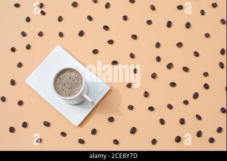 Vista dall'alto composizione di tazza di ceramica bianca con caldo fresco caffè servito su vassoio bianco su superficie beige con sparso chicchi di caffè Foto Stock