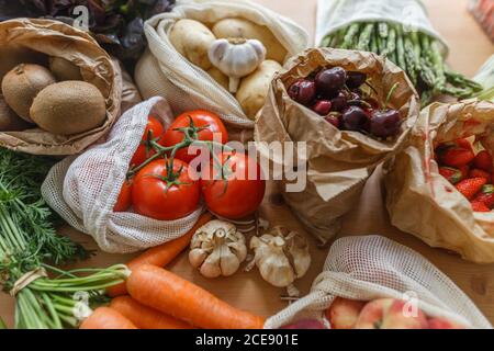 Verdure e frutta assortite in carta e tessuto di cotone a rete confezioni riutilizzabili collocate su un tavolo di legno in cucina Foto Stock