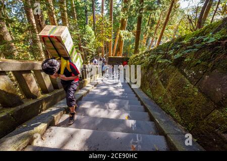 Un uomo duro che lavora consegnando le scatole sulla parte superiore di un tempiale in Nikko in Giappone. Foto Stock