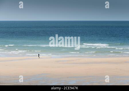 Una persona sola che corre lungo la riva di Fistral Beach a Newquay in Cornovaglia. Foto Stock