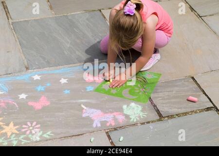 Una bambina di cinque anni si divertiva con l'uso di stencil di plastica per gesso forme su un pavimento di pietra flagstone. Foto Stock