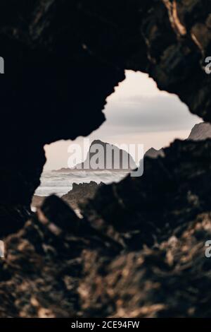 Vista pittoresca della scogliera rocciosa scura tra le onde dell'oceano attraverso la crepa nella roccia sotto il cielo nuvoloso, Portogallo Foto Stock