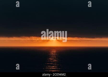 Incredibile paesaggio di cielo nero e acqua dell'oceano increspata con una linea luminosa di cielo dorato del tramonto, Portogallo Foto Stock
