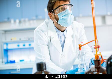 Bel ricercatore in indumenti da lavoro protettivi in piedi in laboratorio e. matraccio di analisi con liquido Foto Stock