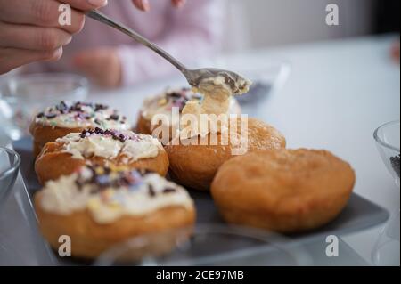 Vista closeup di una donna che decorano deliziose ciambelle vegane fatte in casa con condimento di cioccolato bianco. Foto Stock