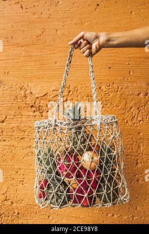 Borsa riutilizzabile in mesh a mano con frutta tropicale fresca naturale su sfondo arancione. Stile di vita senza sprechi. Cibo sano crudo e dieta vegetariana. Foto Stock