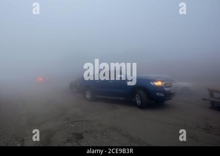 fagaras, romania - 26 GIU 2017: Auto nella nebbia sulla strada transfagarasan 7C. Bassa visibilità, fari non aiutano. Condizioni atmosferiche drammatiche Foto Stock