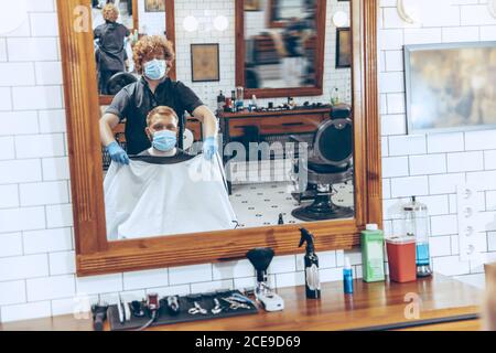 Uomo che ottiene i capelli tagliati al barbiere indossando la maschera durante la pandemia del coronavirus. Guanti professionali da barbiere. Covid-19, concetto di bellezza, autosocura, stile, salute e medicina. Foto Stock