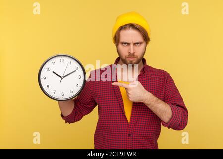 Guardate l'ora! Ritratto di impaziente arrabbiato hipster ragazzo in camicia a scacchi puntando grande orologio e l'aspetto dispiaciuto irritato, mostrando orologi di fretta Foto Stock