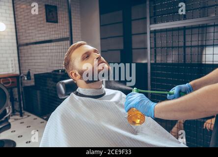Uomo che ottiene i capelli tagliati al barbiere indossando la maschera durante la pandemia del coronavirus. Guanti professionali da barbiere. Covid-19, concetto di bellezza, autosocura, stile, salute e medicina. Foto Stock