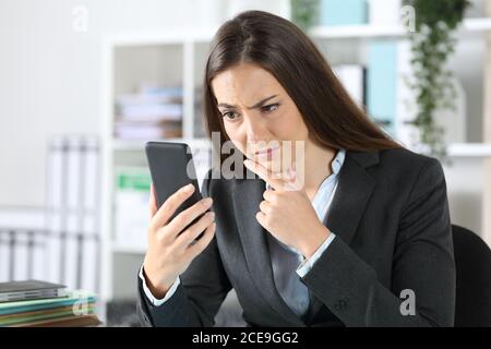 Donna dirigente sospetta che controlla lo smartphone seduto su una scrivania in ufficio Foto Stock