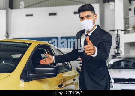 Uomo commerciante di automobile che indossa la maschera medica protettiva sul suo lavoro luogo Foto Stock