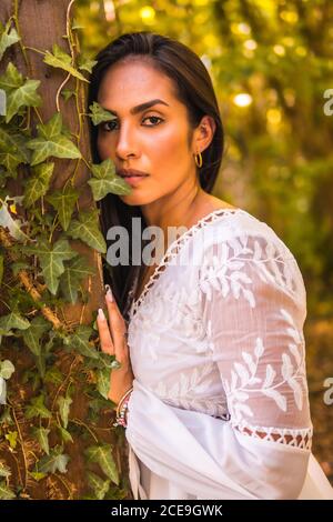 Ragazza bruna latina dai capelli dritti in un bel vestito bianco in un parco in natura Foto Stock