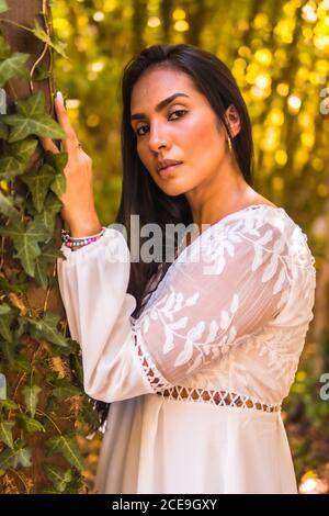 Ragazza bruna latina dai capelli dritti in un bel vestito bianco in un parco in natura Foto Stock