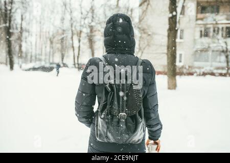 Una foto di una bella giovane vestita di a. giacca invernale nera con zaino in pelle passeggiate nella neve Città con la Th Foto Stock