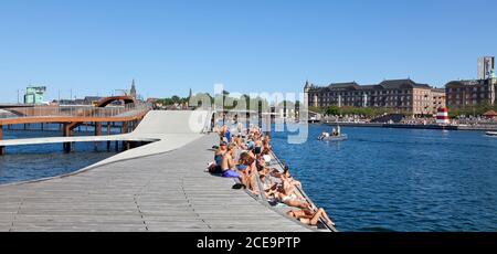 Persone che prendono il sole sulle onde di Kalvebod e le isole ufficiali Brygge Harbour Bath sul lato opposto del canale interno del porto Copenaghen in una giornata estiva Foto Stock