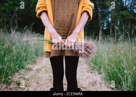 Donna irriconoscibile in piedi nel campo con un mazzo di fiori rustici rosa. Ripresa orizzontale all'aperto. Foto Stock