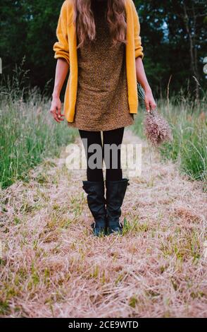 Raccolto verticale di femmina in piedi nel campo con il mazzo di fiori rustici. Foto Stock