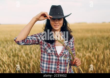 Donna contadina americana che indossa cappello da cowboy, camicia di plaid e jeans al campo di grano Foto Stock