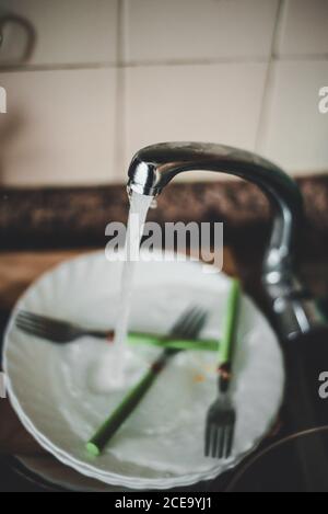 Aprire il rubinetto e lavarlo pieno di piatti sporchi in cucina. Foto Stock