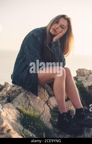 Bella donna rilassante in jeans giacca e sneakers neri e tenendo testa nella natura estiva Foto Stock