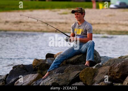 Rock Hall, MD 08/22/2020: Un ragazzo è sulle rocce, con una canna da pesca cercando di catturare il pesce dalla baia di Chesapeake. Indossa jeans e camicia ed è fis Foto Stock