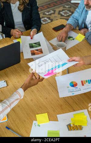 Vista di ritaglio dall'alto del gruppo di lavoratori seduti a. tavolo per riunioni e discussione di schemi e diagrammi in ufficio Foto Stock