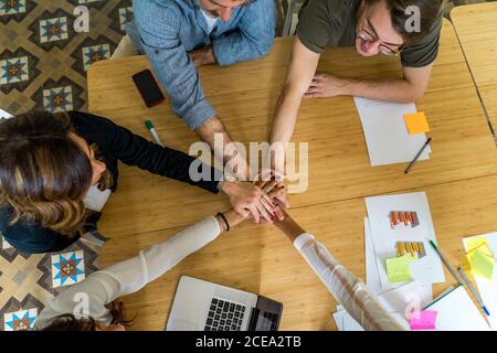 Ritagliare la vista dall'alto dei responsabili dell'ufficio seduti al tavolo e unendosi alle mani durante una riunione Foto Stock