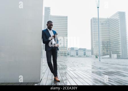 Uomo d'affari afro-americano che usa uno smartphone in piedi all'aperto Foto Stock