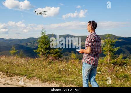 Telecomando drone. Uomo che aziona il controller del copter in montagna. Riprese aeree di Carpathins estivi Foto Stock