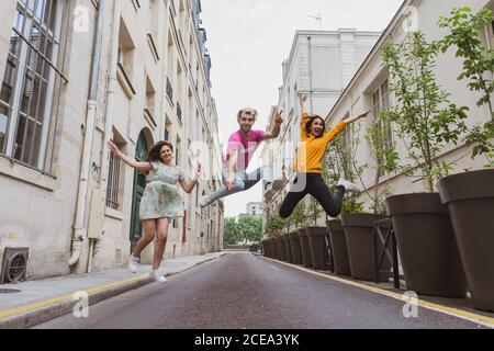 Ridendo giovani donne e trendy uomo in abiti casual saltando Sorvolo in aria su una stretta strada europea Foto Stock