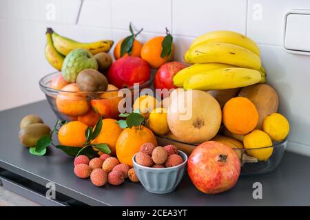 Raccolta di diversi gustosi freschi maturi frutti tropicali in ciotole e piatti sul tavolo vicino a parete Foto Stock