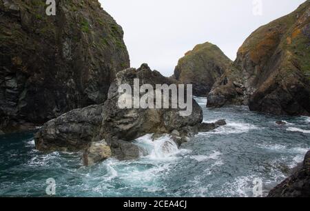 Onde che si infrangono su e intorno rocce vicino al villaggio di pescatori Cornish, Mullion Cove, la penisola di Lizard, Cornovaglia, Regno Unito Foto Stock