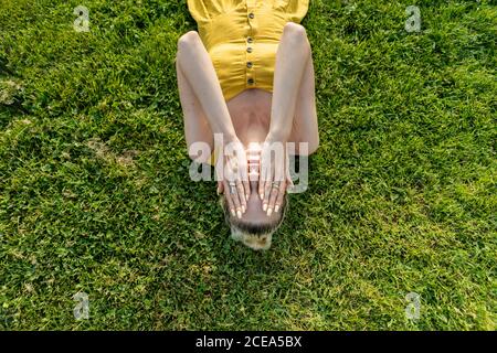 Donna sdraiata sull'erba con le mani sul viso Foto Stock