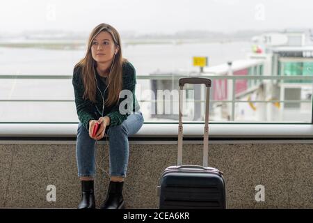 Giovane donna che usa lo smartphone e si siede vicino alla valigia Foto Stock