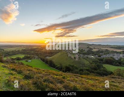 Alba con il sole scoppiare sulla campagna Dorset con il castello di Corfe e le colline che illuminano dal sole del mattino. Foto Stock