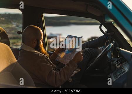 Vista laterale di un uomo adulto che riposa in auto e di una mappa di lettura sul mare. Foto Stock