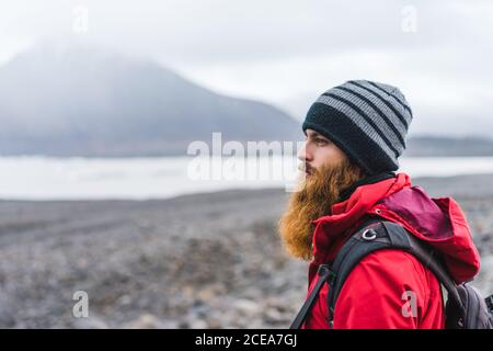 Vista laterale del raccolto bel maschio con i vestiti caldi e zaino in paesaggio montagnoso a Skaftafell, Islanda e Vatnajokull Foto Stock