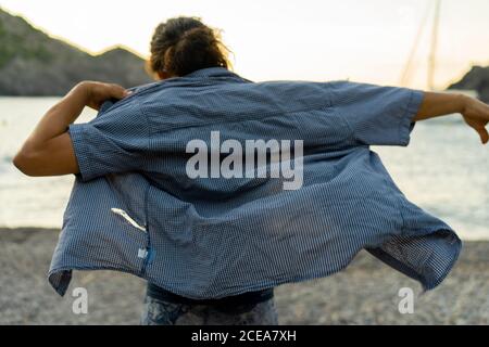 Vista posteriore di un ragazzo che si mette sulla camicia mentre si è in piedi Sulla costa di Tavallera Foto Stock