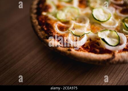 Dall'alto shot di torta yummy con anelli di cipolla e. fette di cetriolo in piedi su tavolo di legno Foto Stock