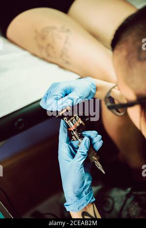 artista tatuaggio irriconoscibile in guanti in lattice che preparano la macchina durante il lavoro in studio Foto Stock