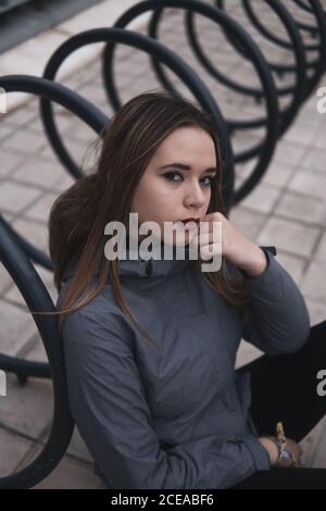 Donna di charme in cappotto e leggini seduti vicino al parcheggio per biciclette Foto Stock