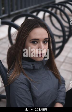 Donna di charme in cappotto e leggini seduti vicino al parcheggio per biciclette Foto Stock