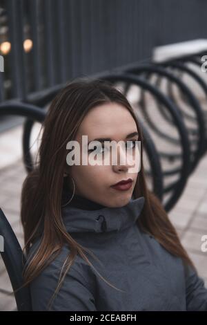 Donna di charme in cappotto e leggini seduti vicino al parcheggio per biciclette Foto Stock