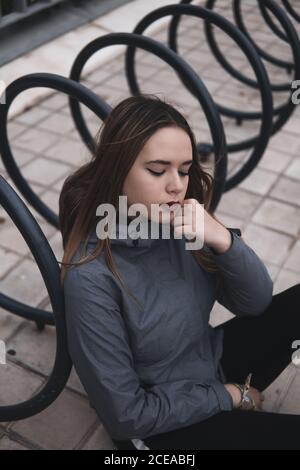 Donna di charme in cappotto e leggini seduti vicino al parcheggio per biciclette Foto Stock