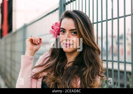 Giovane donna affascinante in maglione con fiore vicino alla griglia Foto Stock